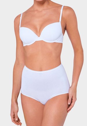 Frau trägt einen weißen gepolsterten BH mit verstellbaren Trägern und weiße Unterwäsche mit hoher Taille vor schlichtem Hintergrund.