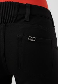 Pantaloni neri con un cinturino testurizzato, tasca posteriore con un emblema decorativo in argento e dettagli di cucitura sottili.