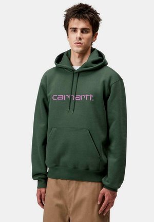 Sudadera verde con bolsillo tipo canguro, que presenta un logo de Carhartt en color rosa. Confeccionada en una tela suave, tiene un corte relajado y capucha ajustable con cordón.