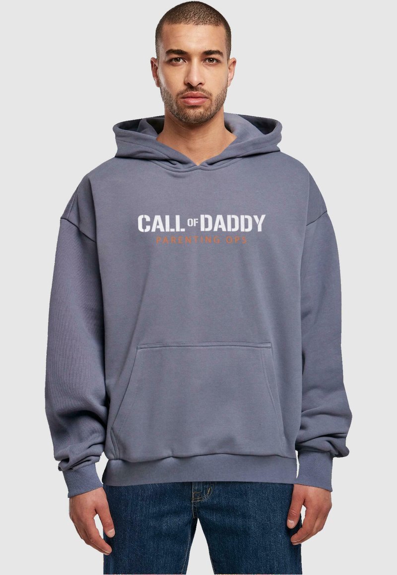 Szara, oversize bluza z kapturem z przednią kieszenią i nadrukowanym tekstem "CALL of DADDY PARENTING OPS" w białym i pomarańczowym kolorze. Tekst umieszczony na środku klatki piersiowej.