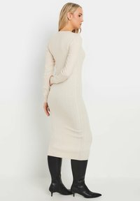 Rippendes, langärmliges beiges Kleid mit taillierter Silhouette, kombiniert mit knielangen schwarzen Stiefeln mit spitzem Zeh. Glatte Textur und dezente Details.