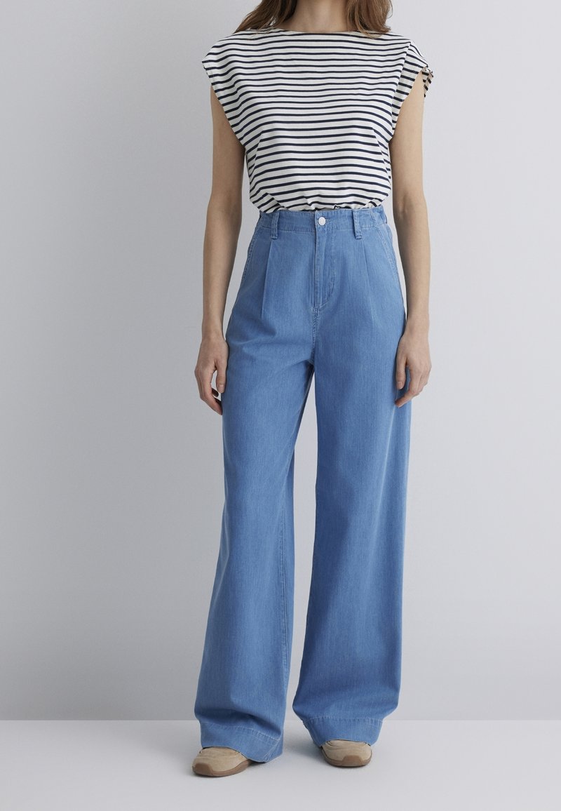 Haut à manches courtes rayé et jean en denim bleu clair taille haute à jambes larges. Comprend une fermeture à boutons à l'avant et deux poches latérales.