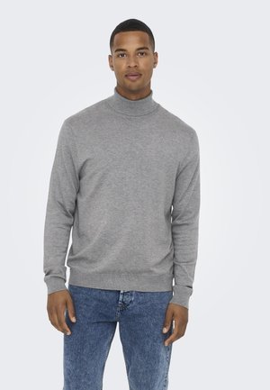 Pull en col roulé gris à manches longues avec une texture douce, col côtelé et poignets ajustés, porté sur un jean en denim bleu.