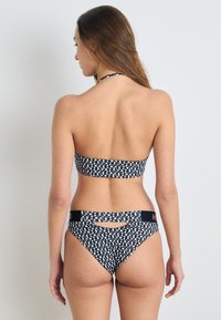 Bikini set u crno-bijelom uzorku s bandeau gornjim dijelom i donjim dijelom niskog struka s izrezom. Materijal je rastezljiv i glatki.