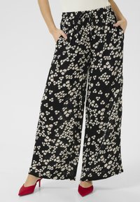 Pantalons larges noirs à motifs floraux avec des fleurs blanches et roses. Fabriqués en tissu léger, avec une taille élastique et des poches latérales.