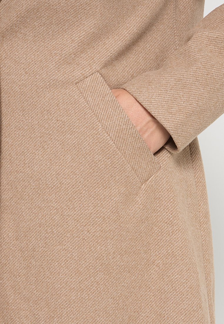 Beige Wollmischungsmantel mit einem dezenten Fischgrätmuster, ausgestattet mit einer Seitentasche und einer glatten Textur.