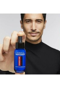 Sérum L'Oréal Men Expert Power Age dans un flacon en verre bleu avec un bouchon compte-gouttes noir. Étiquetage en rouge et blanc.