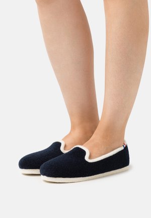 Navy wool slippers with a cream lining, low cut design, rounded toe, and a subtle textured finish; featuring a small tri-color accent at the heel.