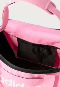 Rózsaszín sporttáska fekete belsővel, cipzáras nyílással és első zsebbel. Masszív fogantyúkkal és feltűnő fehér logóval rendelkezik.