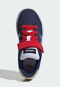 Marineblauwe sneaker met rode veters en band, witte tong met het Adidas-label, en zichtbaar Disney-logo op de binnenzool.
