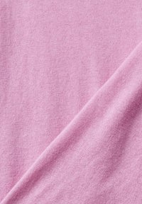 Vaaleanpunainen kangas, jossa on sileä pinta, hienovarainen jousto ja jatkuva neulekuvio, taitettuna kulmasta.