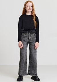 Top nero a maniche lunghe con rifiniture in piume all'orlo, abbinato a jeans in denim neri svasati con una finitura testurizzata. Stivali neri chunky.