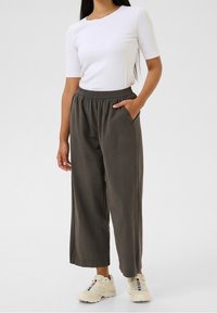 Chemise blanche à manches courtes avec un col rond, associée à un pantalon gris ample doté d'une taille élastique et de poches latérales. Portée avec des baskets blanches.