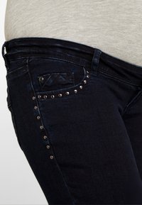 Mörkblå jeans med en tight passform, sidostudsar och en liten framficka. Mjuk tyg med lätt stretch. Ingen synlig slitning eller logotyper.