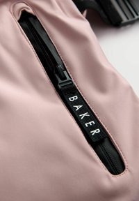 Rozā audums ar gludu tekstūru, kurā ir melna kabata ar rāvējslēdzēju un etiķete ar vārdu "BAKER" baltā krāsā.