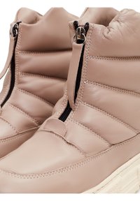 Botas de tobillo de cuero beige con cierre de cremallera, diseño acolchado, punta redondeada y detalles texturizados. Suela de goma plana.