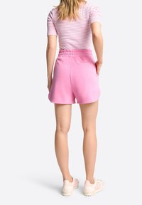 Růžové bavlněné šortky s elastickým pasem a bočními kapsami, které mají volný střih a hladkou texturu. Kombinování s lehkými sportovními botami.