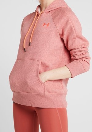 Persoon die een roze Under Armour-hoodie draagt met trekkoorden en een voorzak, gecombineerd met bijpassende roze sportleggings.