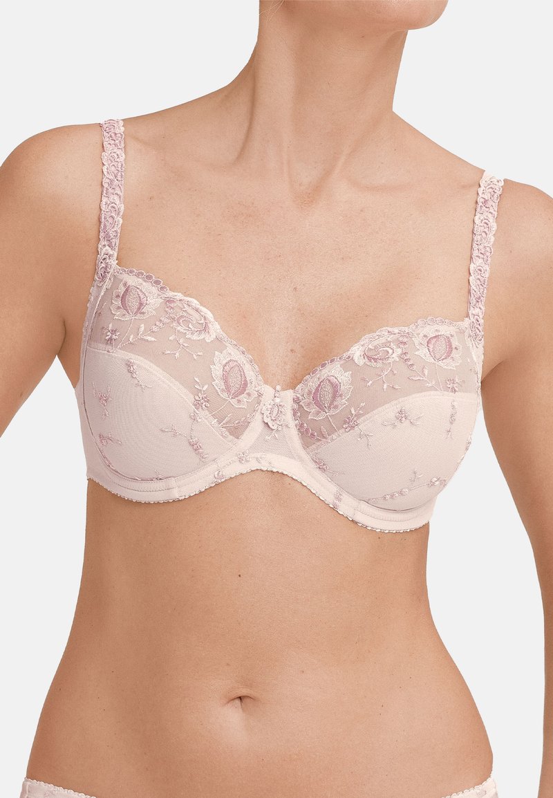 Reggiseno in morbido tessuto beige con delicata ricamo floreale rosa. Presenta spalline in pizzo regolabili e una silhouette liscia e curvata.