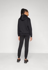 Svart hettegenser med en tettsittende design, justerbar hette og ribbede mansjetter; kombinert med matchende svarte joggebukser med elastiske mansjetter.