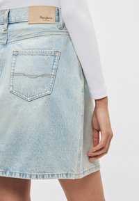 Φούστα από ελαφρύ γαλάζιο τζιν με ελαφρώς ξεφτισμένο τελείωμα, ετικέτα ραμμένη στη μέση και πλάγια πίσω τσέπη σε γωνία. Λείο ύφασμα με χαλαρή εφαρμογή.