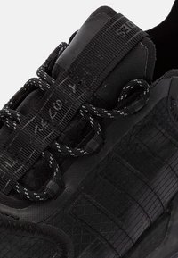 Svart träningssko med ett texturerat mesh-ovandel, hållbar gummisula och kontrasterande svarta och vita snören med ett säkert låssystem.