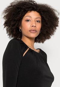 Top preto de manga longa com decote franzido e detalhe recortado nos ombros, com uma textura de tecido lisa e elástica.