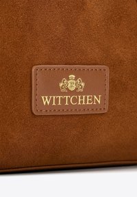 Borsa in suede marrone con una toppa in pelle con il logo “Wittchen” in rilievo dorato, con dettagli di corona e leone.