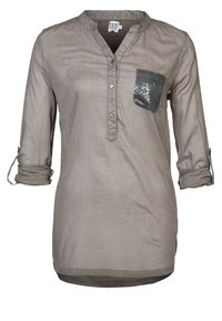 Blusa a maniche lunghe marrone chiaro con scollo a V, patta con bottoni e taschino con paillettes. Tessuto morbido e strutturato con dettaglio maniche arrotolabili.