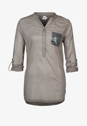 Lichtebruine blouse met lange mouwen, een V-hals, knoopsluiting en een zak met pailletten. Zachte, gestructureerde stof met oprolbare mouwen.