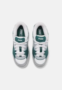 Tenisky Puma se zelenými semišovými akcenty, bílou síťovinou, šedou semišovou špičkou a bílými tkaničkami. Obsahují branding na jazyku a boku. Zaoblený design.