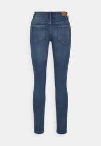 Vaqueros ajustados en denim oscuro con cintura a media altura, diseño de cinco bolsillos y parche de cuero marrón en la parte trasera de la cintura. Textura suave.