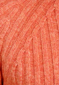 Strickpullover aus weichem korallenfarbenem Garn mit einem strukturierten Ripp- und Kabelmuster, bei dem unterschiedliche Farbschattierungen Tiefe und visuelles Interesse erzeugen.