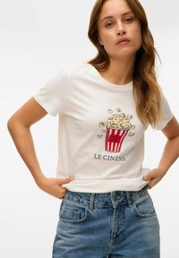 Biała bawełniana koszulka z grafiką czerwono-paskowanego wiadra z popcornem oraz napisem "LE CINÉMA" poniżej. Luźny krój, krótki rękaw.