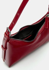 Red leather handbag with a slim design, zip closure, and an adjustable strap. Interior features a black lining and card slot.