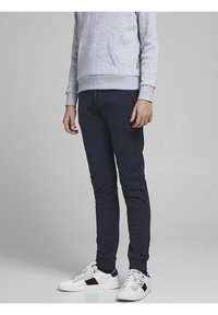 Šedá mikina s přední kapsou, námořnické tepláky s vyšitým logem a bílé tenisky s červenými a námořnickými akcenty.