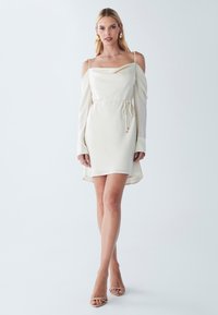 Biela off-shoulder šaty s dlhými rukávmi, stiahnutým pásom a sklápacím výstrihom. Jemná látka s jednoduchou siluetou a bočným rozparkom.