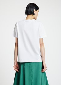 T-shirt en coton blanc à manches courtes, coupe décontractée, col arrondi, porté avec une jupe fluide verte, vue de dos simple.