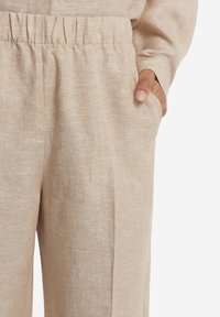 Beige linnedragter med elastisk linning, der har sidelommer og en afslappet pasform, lavet af et lyst, tekstureret stof.