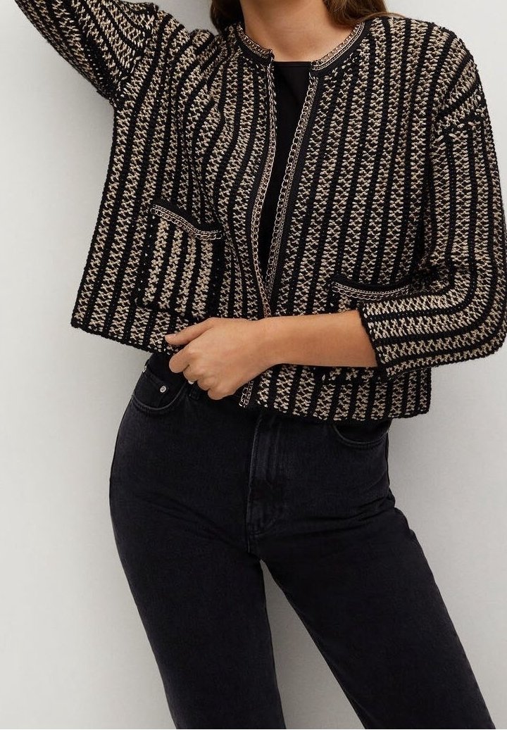 Femme portant un cardigan tricoté à rayures noires et beiges avec des poches à l’avant, par-dessus un haut noir et un pantalon noir.