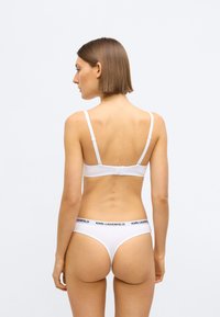 Bílá sada podprsenky a kalhotek s tenkými ramínky a pružným pasem. Materiál je hladký s minimem švů. Logo je umístěno na pasu.
