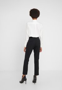 Biała koszula z długim rękawem i kołnierzykiem w połączeniu z dopasowanymi czarnymi spodniami. Modelka nosi czarne botki na obcasie do kostki. Gładki materiał, dopasowany krój.