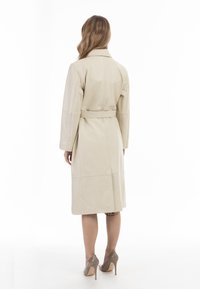 Cappotto trench in pelle beige con cintura in vita, maniche lunghe e tasche laterali, caratterizzato da un design pulito e minimalista e una superficie liscia.