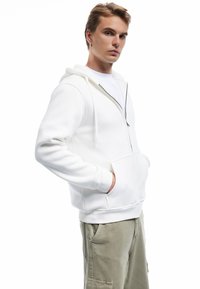 Witte rits hoodie van zachte stof, met een kenguruzak en capuchon met trekkoord, gecombineerd met olijfgroene cargobroek.