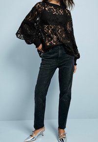 Sort blonde top med lange, luftige ærmer, kombineret med sorte denim jeans med sølvnitter. Modellen har sølvfarvede spidse hæle på.