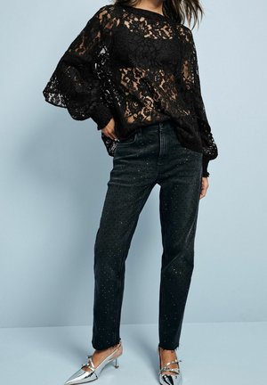 Sort blonde top med lange, luftige ærmer, kombineret med sorte denim jeans med sølvnitter. Modellen har sølvfarvede spidse hæle på.
