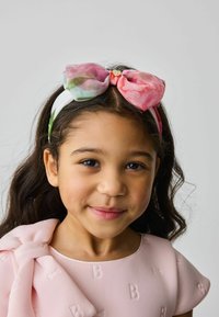 Fascia floreale con un grande fiocco rosa, fissato con un accento dorato. La fascia è bianca e presenta riflessi verdi.