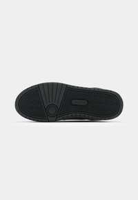 Fekete sneaker talp, texturált gumiból, halszálka mintázattal, kör alakú logóval és hangsúlyos barázdákkal a tapadás érdekében.