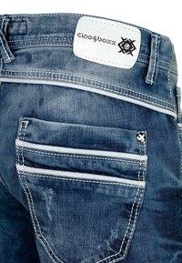 Jean en denim avec une finition bleu foncé délavée. Comprend une étiquette en cuir blanc, deux poches arrière avec un bord blanc et des coutures détaillées.