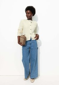 Cardigan en tricot blanc avec des boutons, pantalon large en denim bleu surdimensionné, sac beige matelassé et chaussures à motifs. Textures lisses, coupe décontractée.